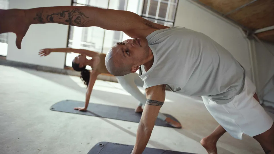 A man doing a yoga pose in a fitness studio with a woman behind him